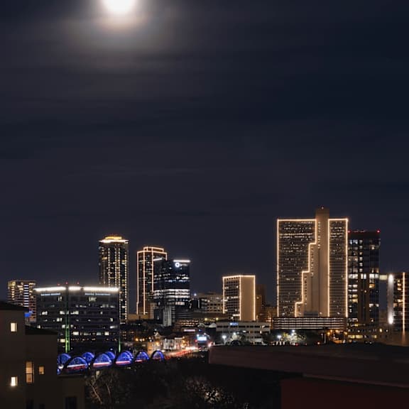 a city skyline at night with a full moon in the sky.