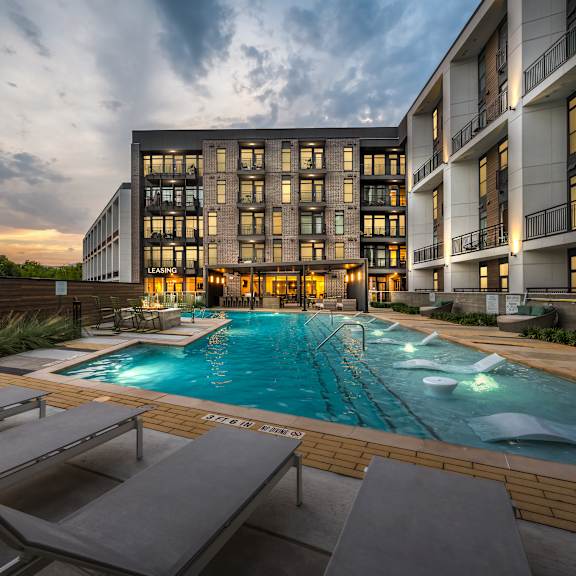 a large swimming pool with lounge chairs and a building in the background