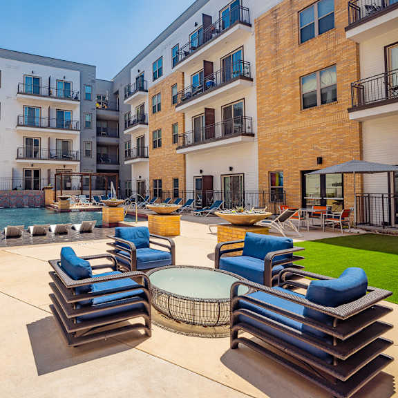 a sunny day at a modern apartment complex with a pool and lounge chairs.