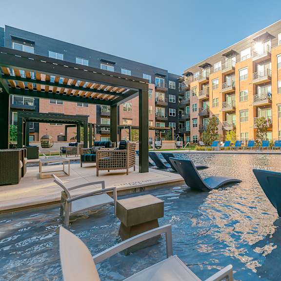 a pool area with a water slide and seating area in front of apartment buildings.