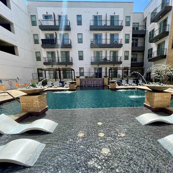 a pool surrounded by a concrete patio and lounge chairs.