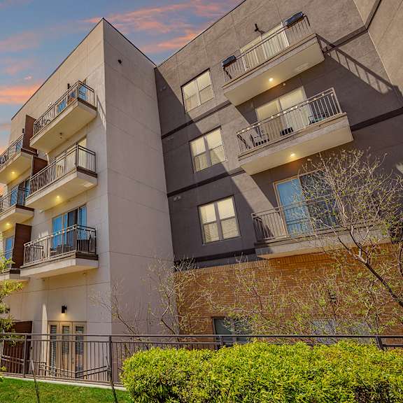 a modern apartment building with balconies and a sunset sky.