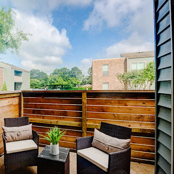 a patio with two chairs and a table with a potted plant on it.