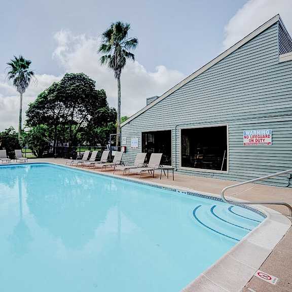a large swimming pool with lounge chairs and a building in the background.
