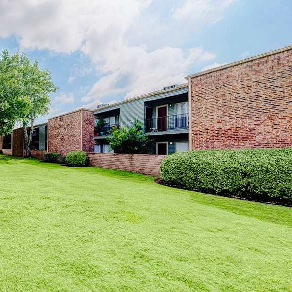 a large grassy area in front of a building with a tree on the left.