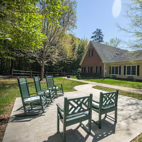 a sunny day at a park with a bench and a building in the background.at spring arbor of williamsburg, virginia