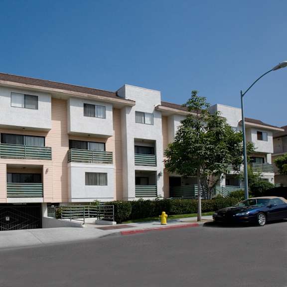 a black car is parked on the street in front of a white apartment building.