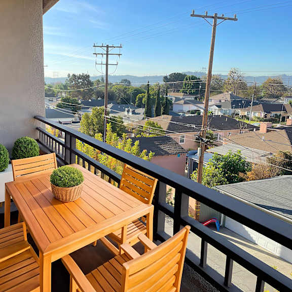 a wooden table and chairs on a balcony with a view of the neighborhood.