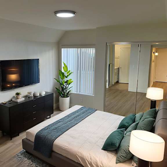a bedroom with a bed, nightstand, and a plant.