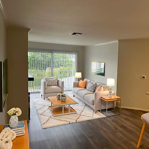 a living room with a grey couch, a coffee table, and a window with blinds.