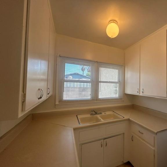 a kitchen with white cabinets and a window with blinds.