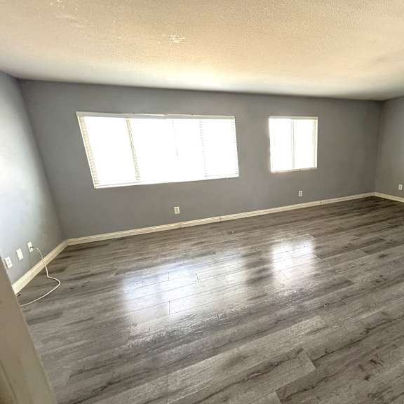 a room with grey flooring and two windows.