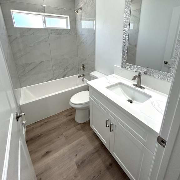 a white bathroom with a marble wall and a wooden floor.