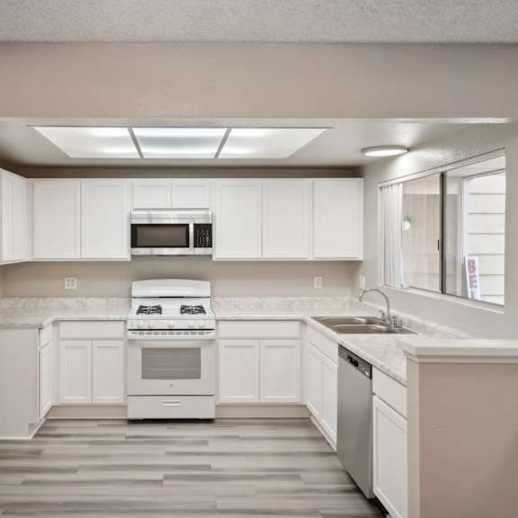 an empty kitchen with white cabinets and a window
