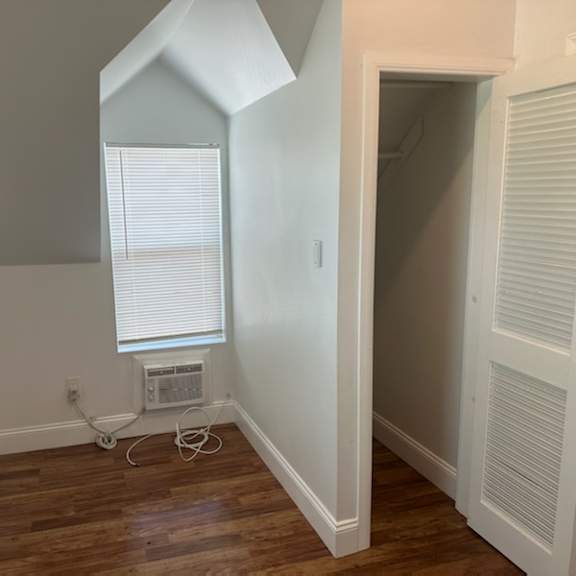 a room with a window and a wooden floor and an air conditioner
