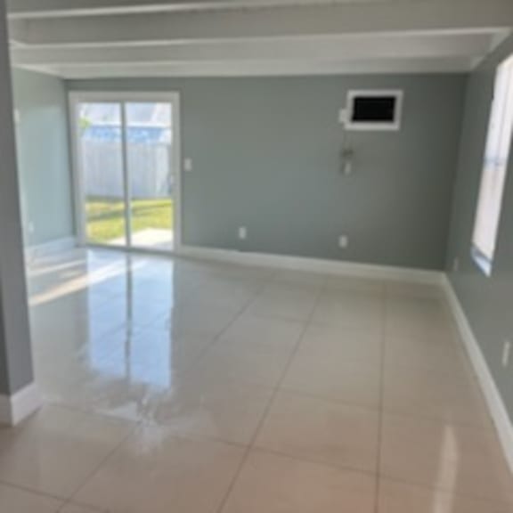 an empty living room with a tile floor and a door to a balcony