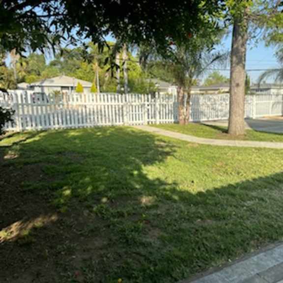 a yard with a white fence and a sidewalk