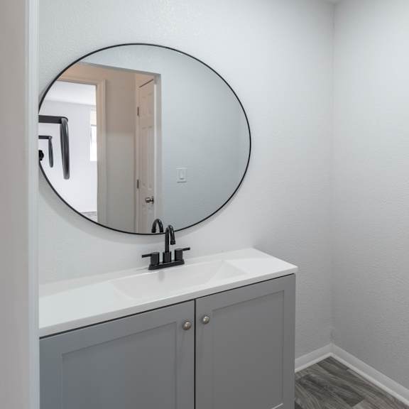 a bathroom with a round mirror above a sink. at red bay apartment complex, jacksonville, fl, 32211