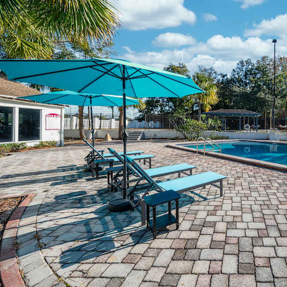 a pool area with a blue umbrella and a brick patio. at red bay apartment complex, jacksonville, fl, 32211