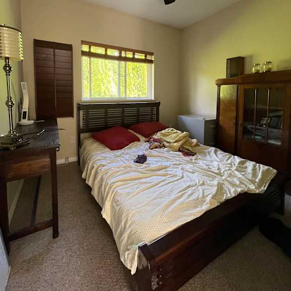a bed with white sheets and a red pillow is in a room with a ceiling fan.