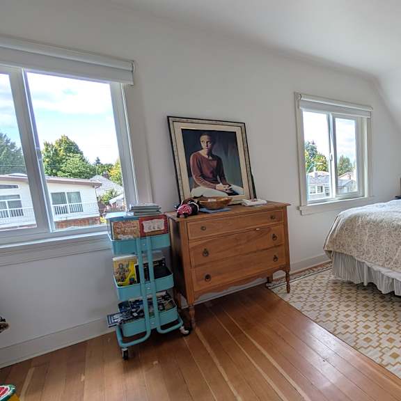 a bedroom with a bed, dresser, and a window overlooking a residential area.