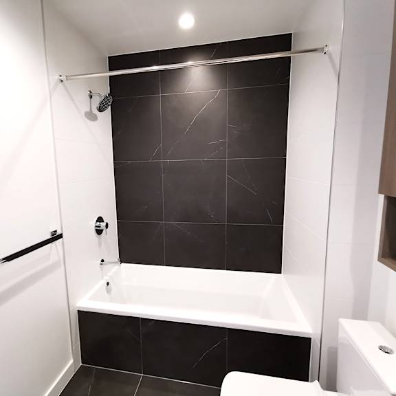 a white bathroom with black tiles and a white bathtub.