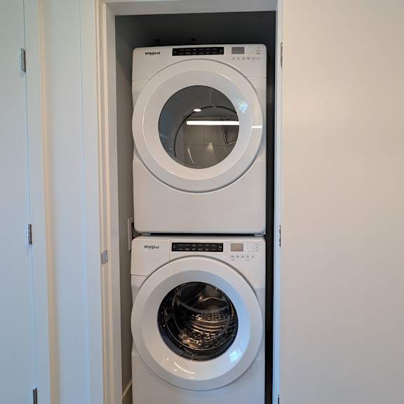 a white dryer is stacked on top of a white washing machine in a small laundry room.