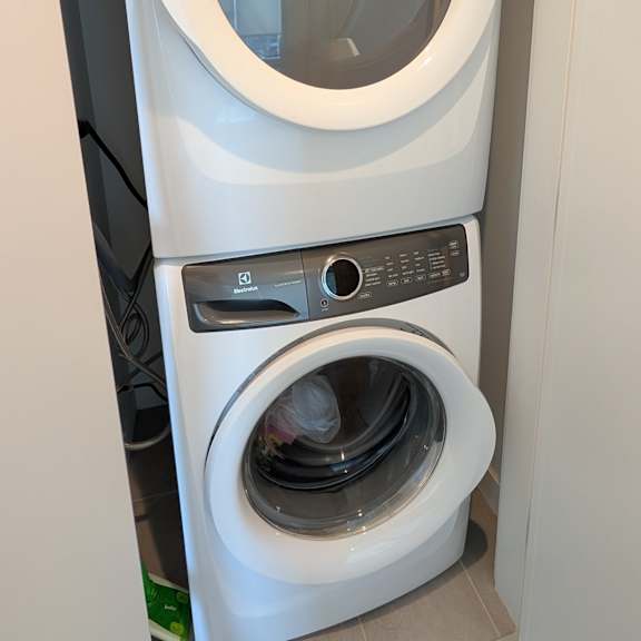 a white front loading washing machine with a black control panel is stacked on top of a black front loading washing machine.