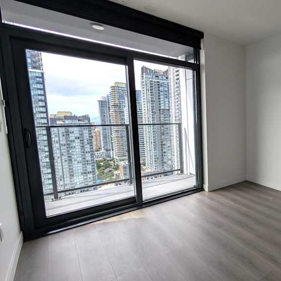 a room with a sliding glass door leading to a balcony with a view of a city skyline.