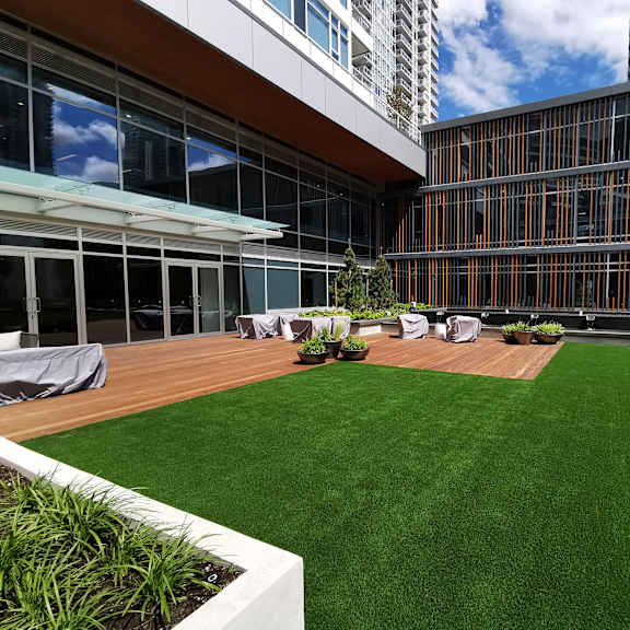 a large grassy area in front of a building with a wooden deck and a white planter box.