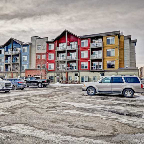 a parking lot with cars and a multi-story apartment building in the background.