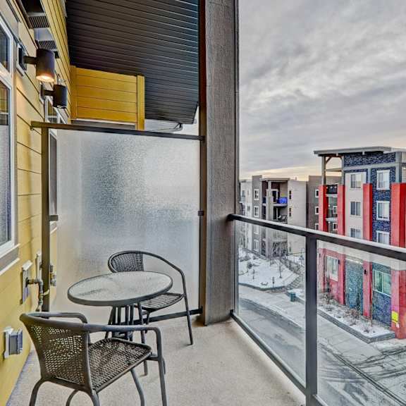 a balcony with a table and chairs overlooks a snowy street.
