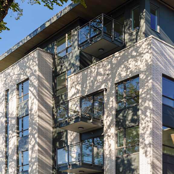 a modern building with a balcony and a tree in the foreground.