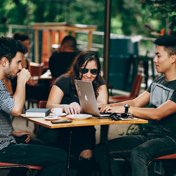 three people sitting at a table with laptops.