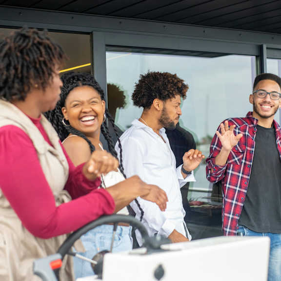 four people are standing in front of a grill, smiling and laughing together.