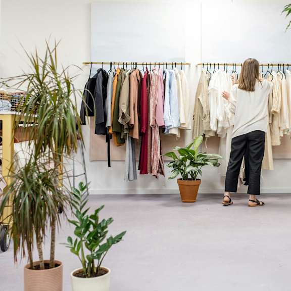 a woman is looking at clothes on a rack in a room with potted plants.