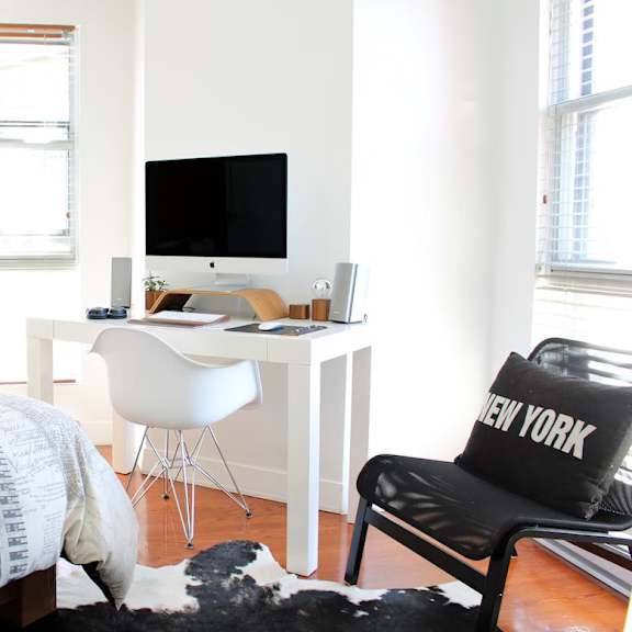 a black and white cowhide rug sits in front of a white bed and a white desk with a computer on it.