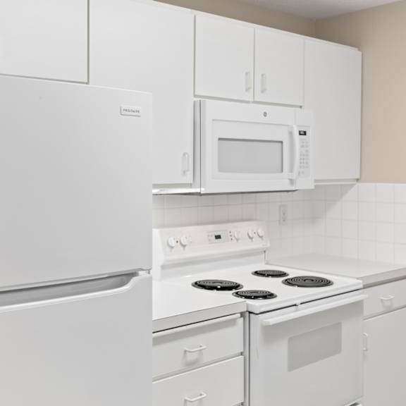 a white kitchen with a refrigerator, microwave, oven, and stove.