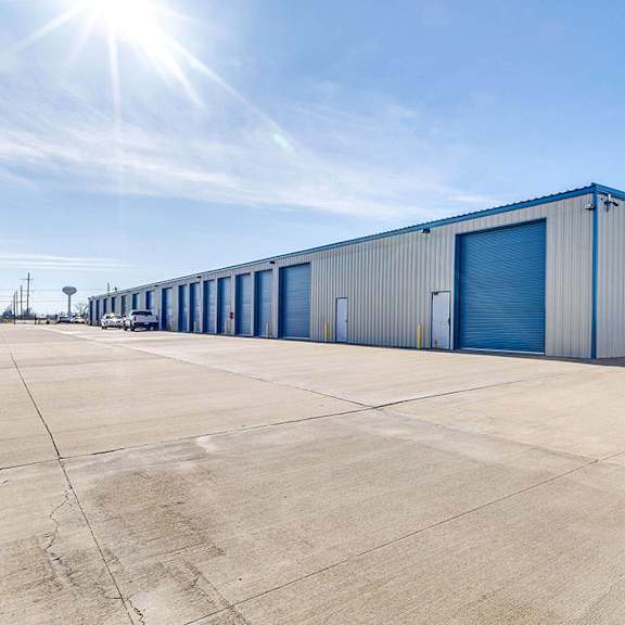 a large industrial building with a blue door is surrounded by a parking lot.