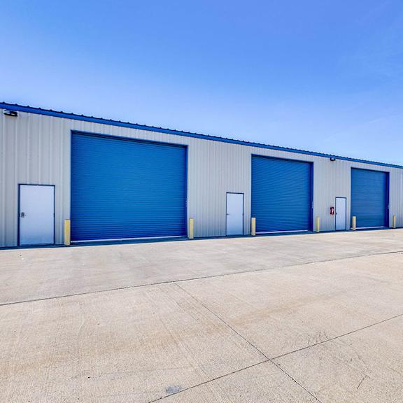 a long row of storage units with blue doors and a white car parked in front.