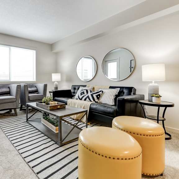 a living room with a black couch, a coffee table, and a shelf with various items.