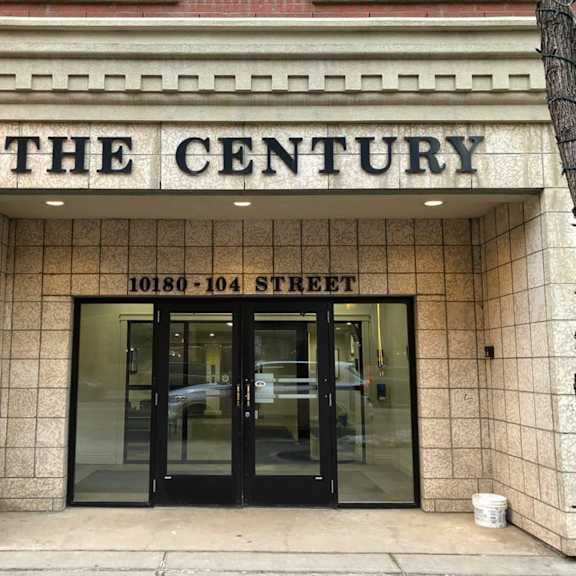the century building at 10180 104th street has a black door and a white bucket on the sidewalk.