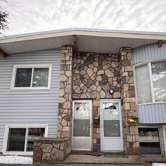 a house with a grey siding and a stone pillar in front.