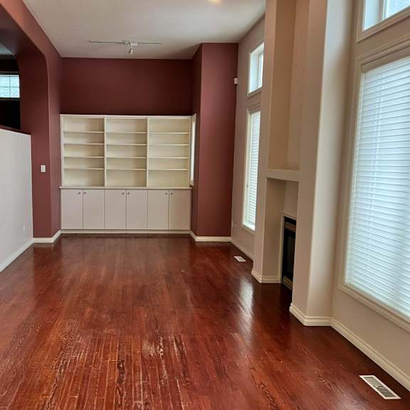 a room with wooden floors and a wall with a window covered with blinds.