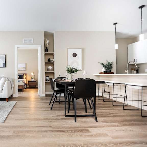 a modern living room with a white sofa, a black dining table, and a kitchen area in the background.