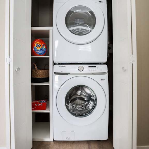 a white dryer is on top of a white washing machine in a small laundry closet.
