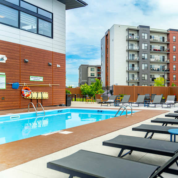 a pool with sun loungers and apartment buildings in the background.