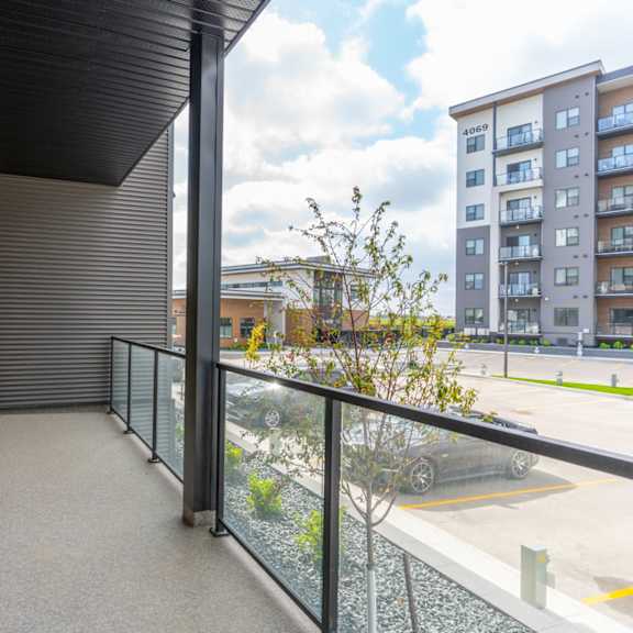 a balcony with a glass railing and a tree in the background.