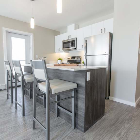 a kitchen with a refrigerator, microwave, and bar stools.