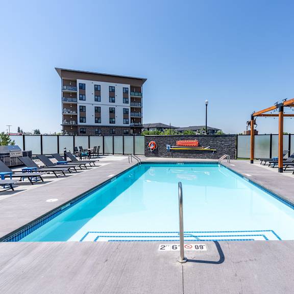 a large swimming pool with a diving board and lounge chairs.